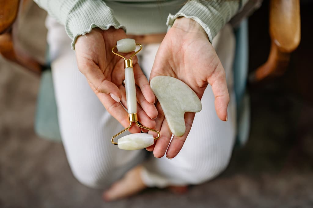 Japanese Skincare 3 A woman kneels and has her hands open to show a jade roller and a jade color Guasha, whose use is a recommended step in the japanese skincare process
