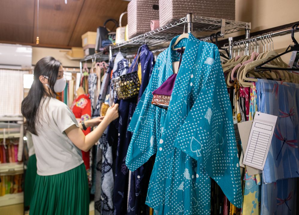 Kimono Rental 5 Young woman looking at three kimono in blue, white, and teal in a kimono rental shop