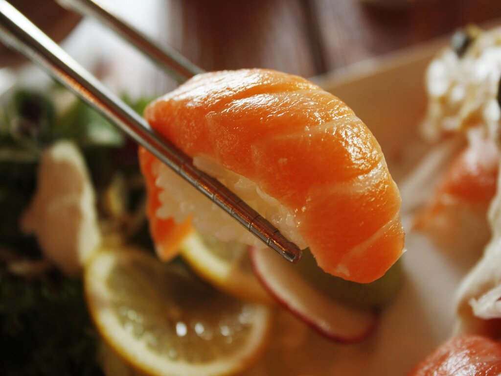 At an authentic sushi restaurant, a close-up shot of salmon sushi, picked by the chopsticks.