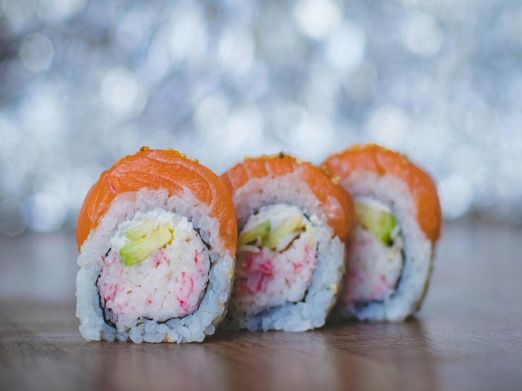 Three western style sushi rolls lining.On top there is salmon, and in it it has avocado, surimi and cream cheese.