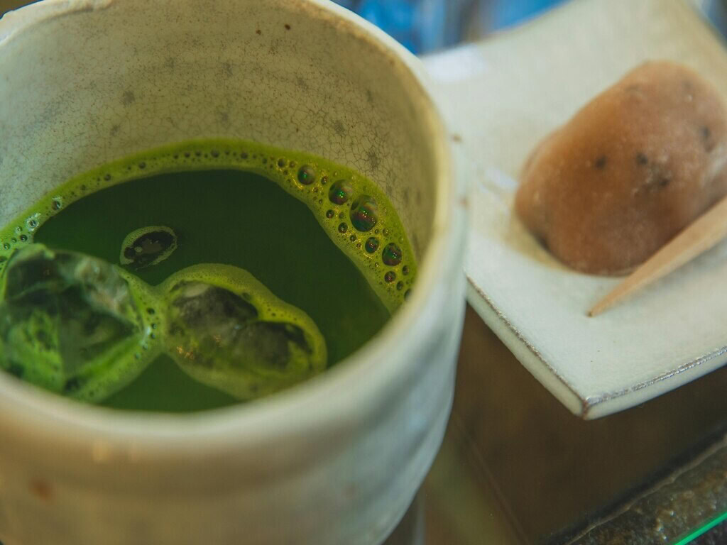 A close up photo of a glass of matcha with ice on the left side and Japanese confectionary on the right side.