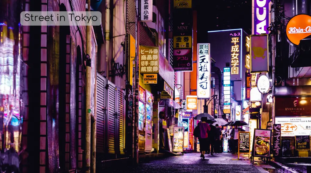 An image of a street in Tokyo at night with people walking under their umbrellas